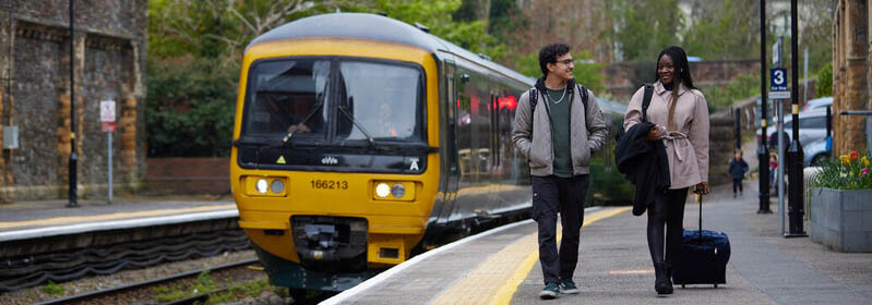 Two students walk down a platform as a train approaches